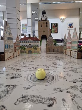 Minigolfbahn mit Modellhäusern und einem gelben Ball im Vordergrund in einem Innenraum