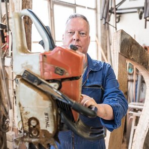 Künstler Volker W. Hamann ist mit einem blauen Arbeitsanzug bekleidet und bedient eine Maschine.