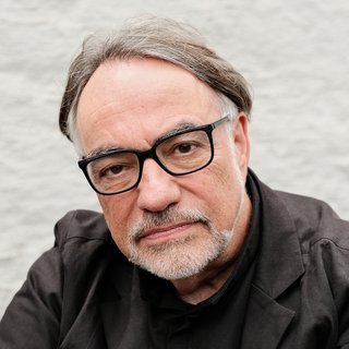 Portraitaufnahme von Natan Sznaider. Er hat einen kurzen Bart, trägt eine Brille und ist mit einem schwarzen Hemd bekleidet. Er blickt direkt in die Kamera.