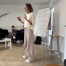 Melanie Müller von niessnerdesign steht vor einem Flipchart und scheint mit jemandem zu sprechen. Sie gestikuliert mit den Händen.