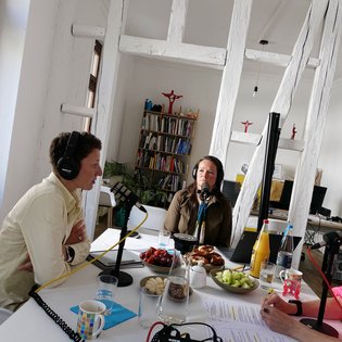 Gästin Dr. Cornelie Kunkat (Deutscher Kulturrat) und Gästin Sabrina Haane (SWR Symphonieorchester) bei der Podcast-Aufnahme. Sie tragen beide Kopfhörer und haben je ein Tischmikrofon vor sich.
