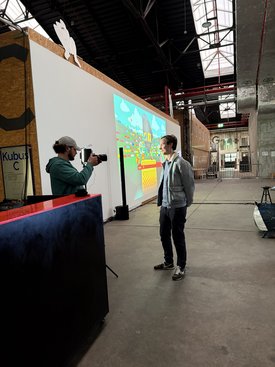 Ein Mann spricht auf einem Symposium über Kunst im Spiel, während ein anderer Mann ihn filmt.