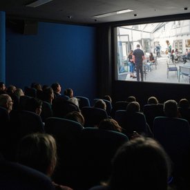 Blick von hinten über die voll besetzten Kino-Stuhlreihen hinweg auf die Leinwand, auf der einer der Kurzfilme läuft.
