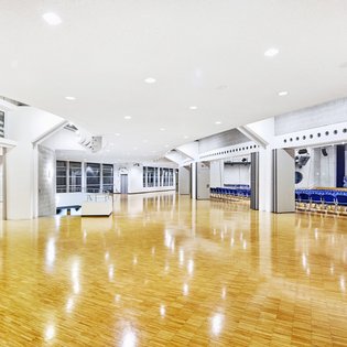 Innenansicht auf das Foyer und den unbestuhlten Kombisaal. Die Wände sind in hellen Tönen gehalten, der Saal verfügt über einen Parkettboden. Hinten im Saal ist eine Bühne zu sehen