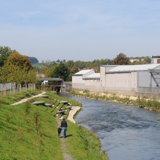 Foto: Blick auf die terassenförmig angelegten Sitz- und Liegemöglichkeiten an der Fils. Auf der anderen Seite der Fils sind Hallen wie von einer Fabrik zu sehen.