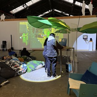 Personen betrachten eine digitale Kunstinstallation auf einem Symposium in einer industriellen Halle.