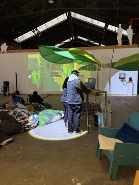 Personen betrachten eine digitale Kunstinstallation auf einem Symposium in einer industriellen Halle.