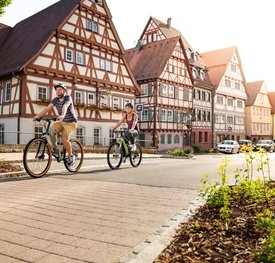 Blick auf eine Strasse mit Fachwerkhäusern. Zwei Radfahrer sind unterwegs.