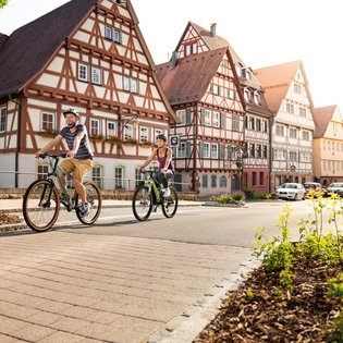 Blick auf eine Strasse mit Fachwerkhäusern. Zwei Radfahrer sind unterwegs.