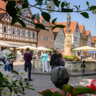 Blick auf einen Brunnden. Davor stehen Menschen, die an einer Stadtführung teilnehmen.