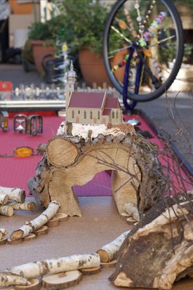 Miniaturkirche auf einem Holzstamm mit Birkenholzscheiben und einem Fahrrad im Hintergrund