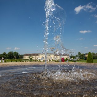 Blick auf das Schloss. Im Vordergrun ein Springbrunnen.