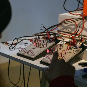 Person vor zwei Steckbrettern mit elektronischen Bauteilen und leuchtenden LEDs auf einem Tisch