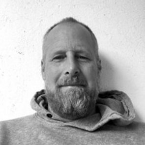 Schwarzweiß-Portrait von Paul Petry. Er ist mit einem Hoodie bekleidet, trägt Bart und lächelt in die Kamera.
