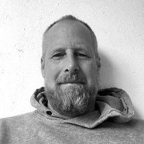 Schwarzweiß-Portrait von Paul Petry. Er ist mit einem Hoodie bekleidet, trägt Bart und lächelt in die Kamera.