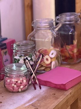 Gläser mit bunten Süßigkeiten und Zangen stehen auf einem Tisch neben pinken Servietten beim Kunst-im-Game-Symposium.