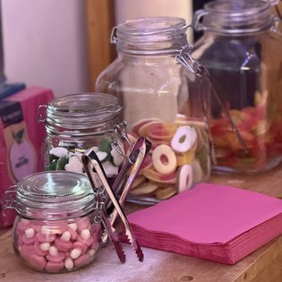 Gläser mit bunten Süßigkeiten und Zangen stehen auf einem Tisch neben pinken Servietten beim Kunst-im-Game-Symposium.