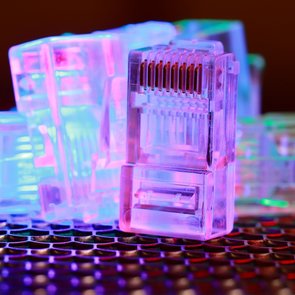 Mehrere transparente RJ45-Stecker liegen auf einer schwarzen, strukturierten Oberfläche und sind mit buntem Licht beleuchtet
