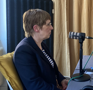 Gästin Prof. Dr. Angela Borgstedt während der Aufnahme des Podcast. Sie sitzt an einem Tisch, trägt Kopfhörer und hat ein Tischmikrofon vor sich stehen.