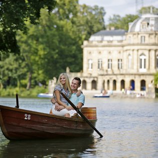 Blick über den See auf Monrepos. Ein Paar fährt Boot auf dem See.