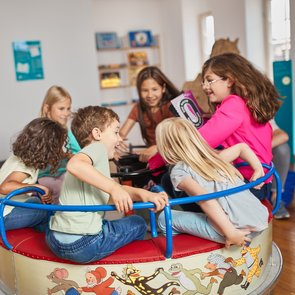 Mehrere Kinder sitzen auf einem Karussell, welches sich gerade dreht.
