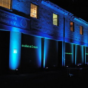 Aussenansicht blaues Haus. Die Fassade ist mit blauem Licht beleuchtet.