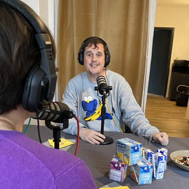 Moderator Ingmar Volkmann während der Aufnahme des Podcast. Er sitzt an einem Tisch, trägt Kopfhörer und hat ein Tischmikrofon vor sich stehen.