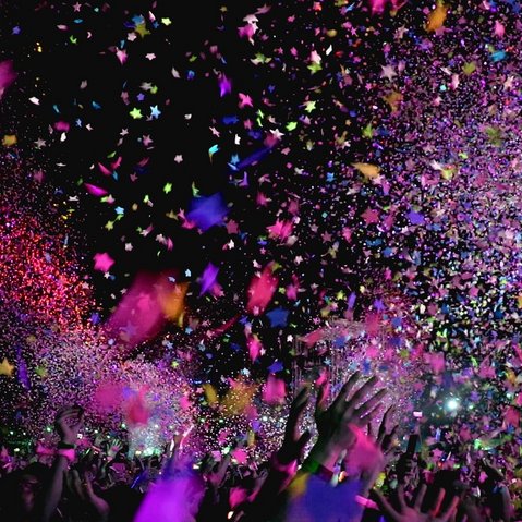 Bild von nur verschwommen sichtbaren Kindern beim Feiern auf einem Konzert oder einer Party. Konfetti rieselt von der Decke. 