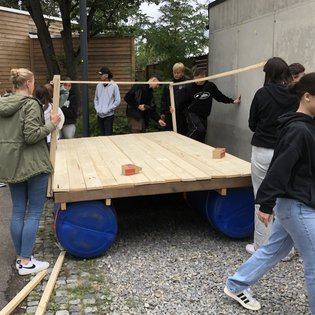 Eine Gruppe Jugendlicher baut aus Tonnen und Holz ein Floß.
