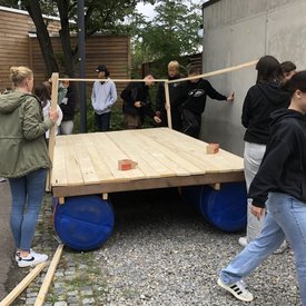 Eine Gruppe Jugendlicher baut aus Tonnen und Holz ein Floß.