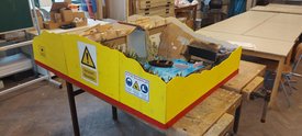 Modell einer Minigolfbahn mit gelb-roter Umrandung und Wasserhindernis auf Werkbank in Werkstatt.