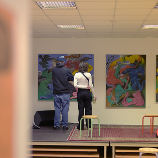 Zwei Personen stehen mit dem Rücken zur Kamera vor einer Wand und betrachten ein Gemälde.