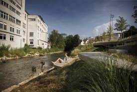 Foto: Blick auf die terassenförmig angelegten Sitz- und Liegemöglichkeiten an der Fils. Auf der anderen Seite der Fils ist ein großes Gebaüde zu sehen. Ein Kind Spielt im Wasser, eine Frau, vermutlich die Mutter, schaut vom Ufer aus zu
