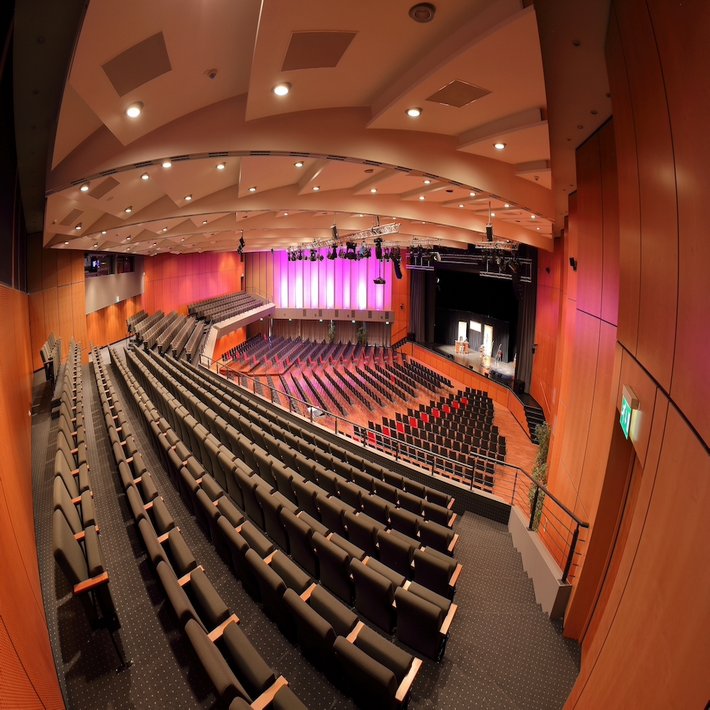 Innenansicht der Kongresshalle: über Stuhlreihen hinweg wird auf eine Bühne geblickt.