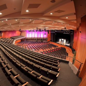 Innenansicht der Kongresshalle: über Stuhlreihen hinweg wird auf eine Bühne geblickt.