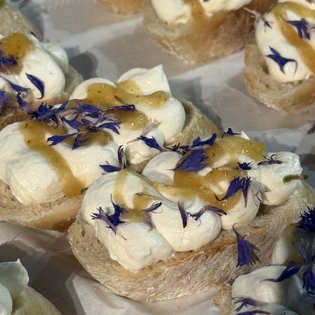 Häppchen mit Sahne und essbaren Blüten sind kunstvoll auf einer Servierplatte angerichtet.