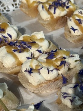 Häppchen mit Sahne und essbaren Blüten sind kunstvoll auf einer Servierplatte angerichtet.