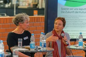 Dr. Birte Werner und Jule Fiedler auf dem Podium,im Hintergrund zeigt ein Bildschirm den Titel: Sparen wir uns kaputt?