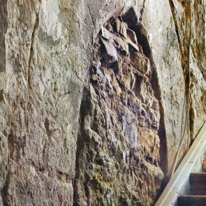 Eine rekonstruierte historische Wand mit einem freigelegten Spitzbogen und einer Treppe daneben.