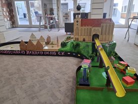 Minigolfbahn mit Modell einer Kirche, grüner Landschaft und bunten Hindernissen in einem Innenraum