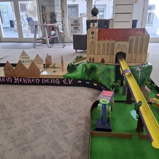 Minigolfbahn mit Modell einer Kirche, grüner Landschaft und bunten Hindernissen in einem Innenraum