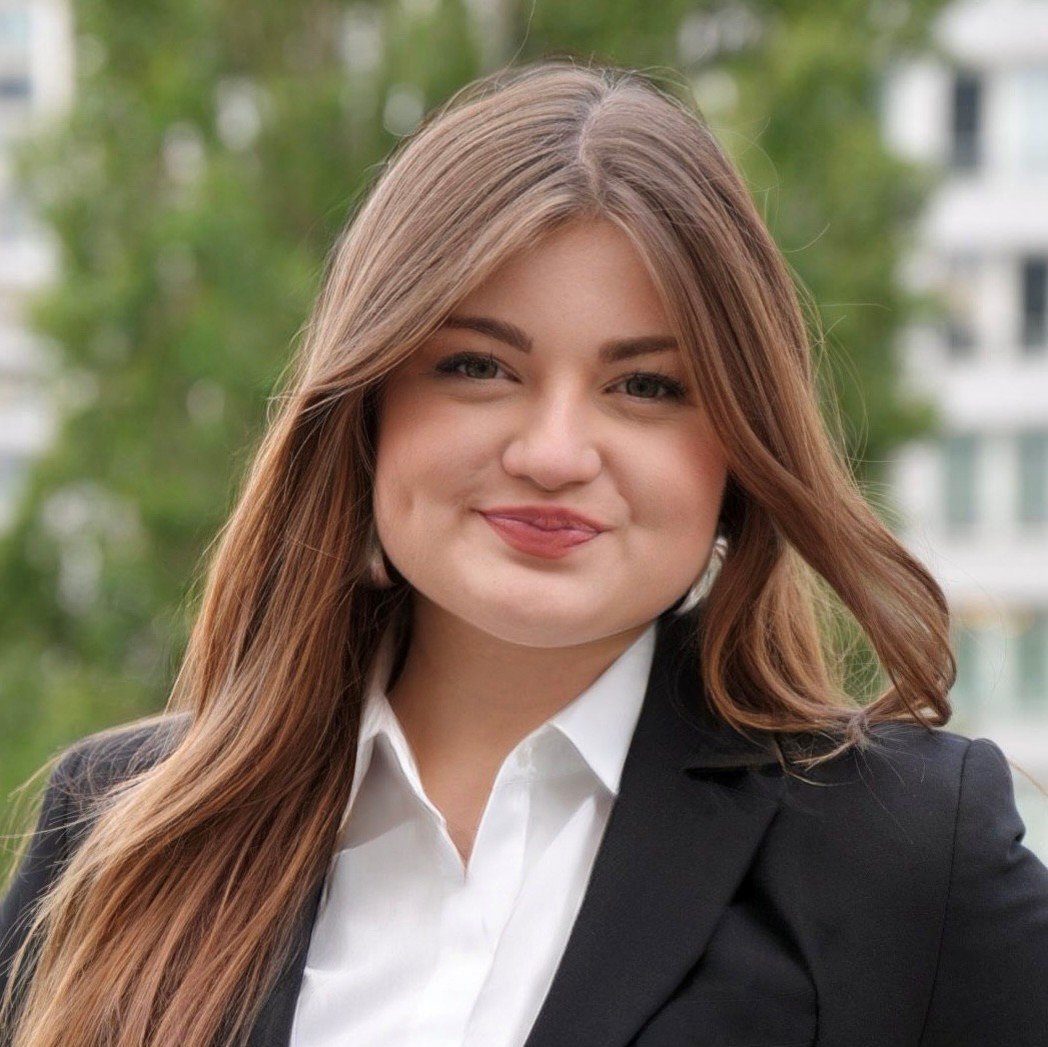 Porträt einer jungen Frau mit langen glatten Haaren, weißem Hemd und schwarzem Blazer vor unscharfem Hintergrund