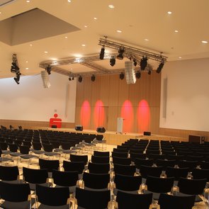 Innenansicht auf einen bestuhlten Raum und eine Bühne.