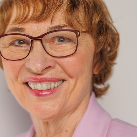 Portrait von Susanne Wetterich. Frau Wetterich hat halblanges braunes Haar und trägt eine Brille. Auf dem Bild ist sie mit einem rosa Blazer bekleidet.