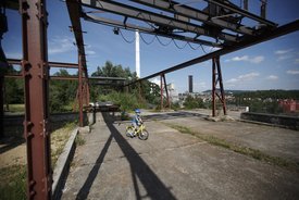 Ein kleines Kind fährt Fahrrad zwischen stillgelegten Bergbauanlagen im Travertinpark. Im Hintergrund öffnet sich der Blick auf ein Tal