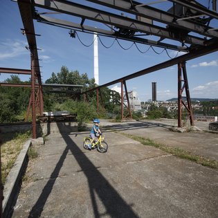 Ein kleines Kind fährt Fahrrad zwischen stillgelegten Bergbauanlagen im Travertinpark. Im Hintergrund öffnet sich der Blick auf ein Tal
