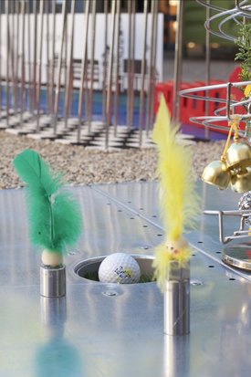 Minigolfball in Loch auf Metallplatte mit zwei Metallstiften, die grüne und gelbe Federn tragen