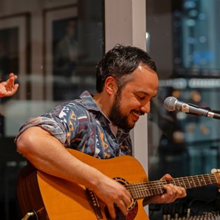 Mann mit gemustertem Hemd spielt akustische Gitarre vor Mikrofon in Innenraum