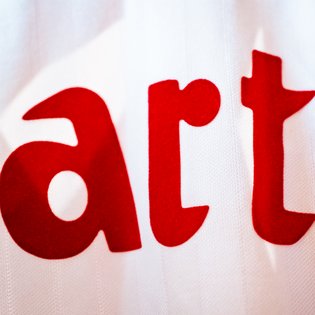 Großaufnahme roter, fetter Buchstaben 'a', 'r' und 't' auf weißem Stoff. Ausschnitt aus einem Trikot des VfB Stuttgart.