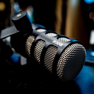 Nahaufnahme eines schwarzen Rode-Mikrofons mit Metallgitter und Halterung vor unscharfem Hintergrund.